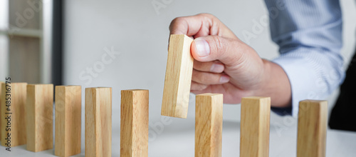 Risk and strategy in business, Close up of business woman hand gambling placing wooden block on a line of domino