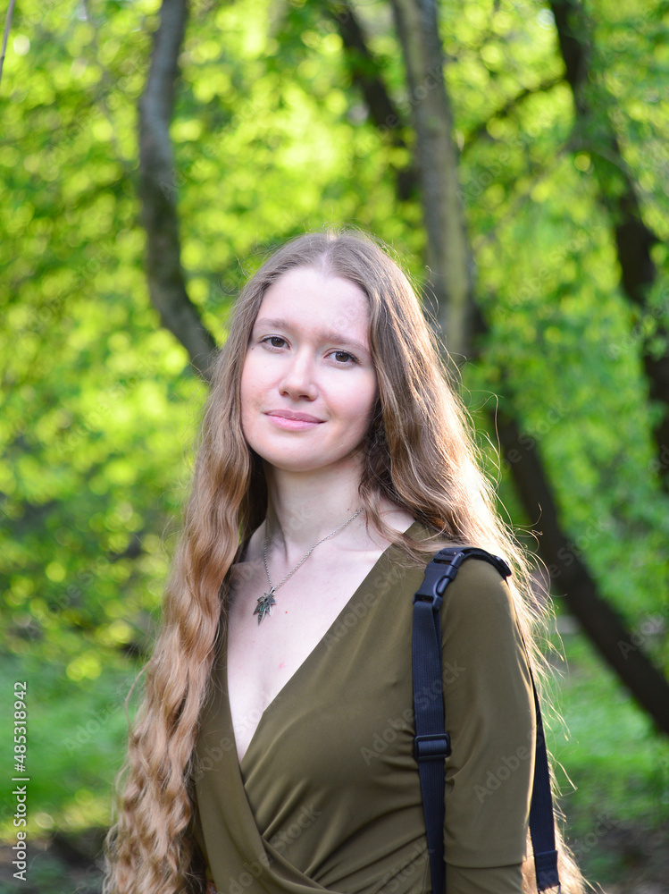 Beautiful young blonde long haired woman in green dress with gothic weed pendant necklace in the spring park. Twisted bokeh formed by green leaves in the sunlight Beautiful young blonde long haired woman in green dress with gothic weed pendant necklace in the spring park. Twisted bokeh formed by green leaves in the sunlight
