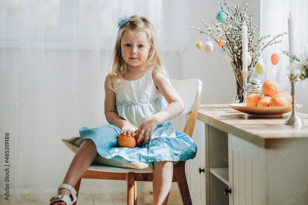 Obraz premium Preparation for the Easter holiday. A little girl is sitting on a chair in a room with fruits in her hands in anticipation of the holiday.