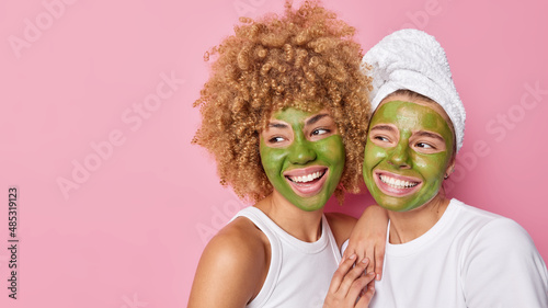 Valokuva Horizontal shot of happy women apply green nourishing masks on face look gladful