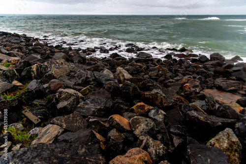 Foto A view of the sea crashing its waves to the beach rocks on a gloomy weather in R