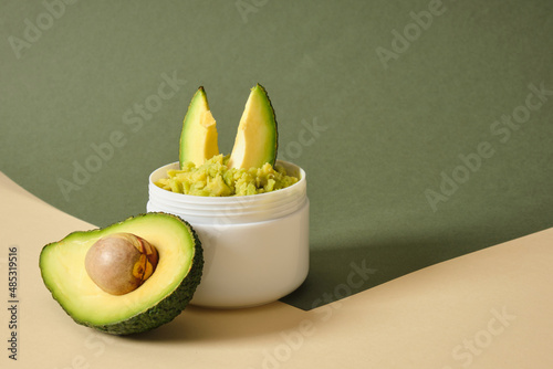avocado half and white mockup blank jar with avocado puree on wooden stand, green background photo