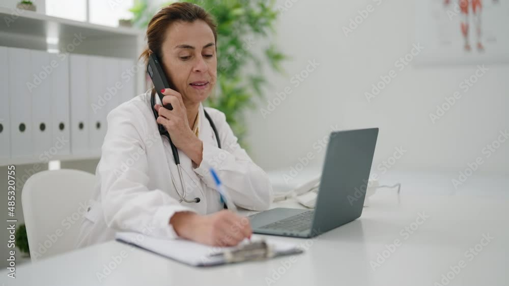 Middle age woman wearing doctor uniform talking on the smartphone at clinic Middle age woman wearing doctor uniform talking on the smartphone at clinic