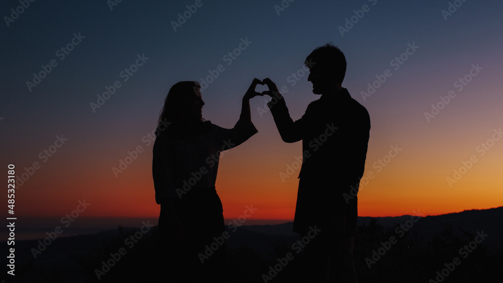 Silhouette of boy and girl in love make heart symbol 