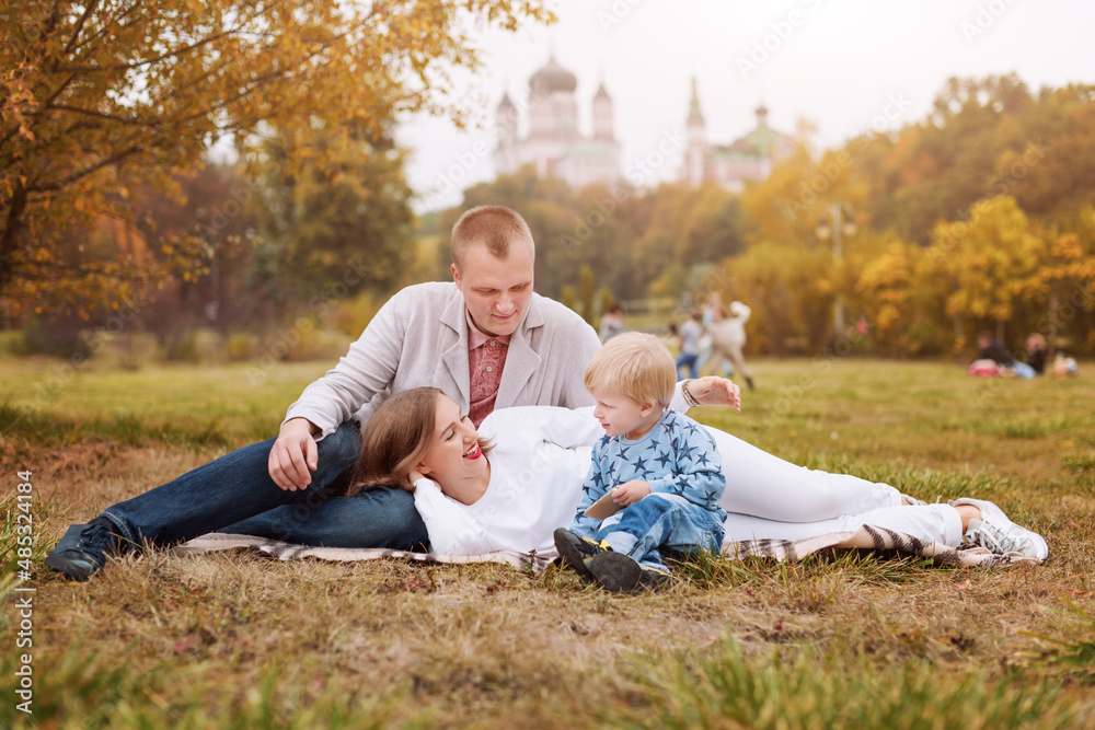 Happy family with child in autumn park sitting on a plaid.