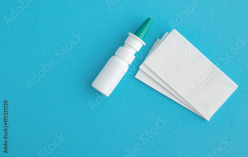 A spray bottle with nose drops and paper napkins on a blue background. The concept of colds, flu and runny nose. Copy space