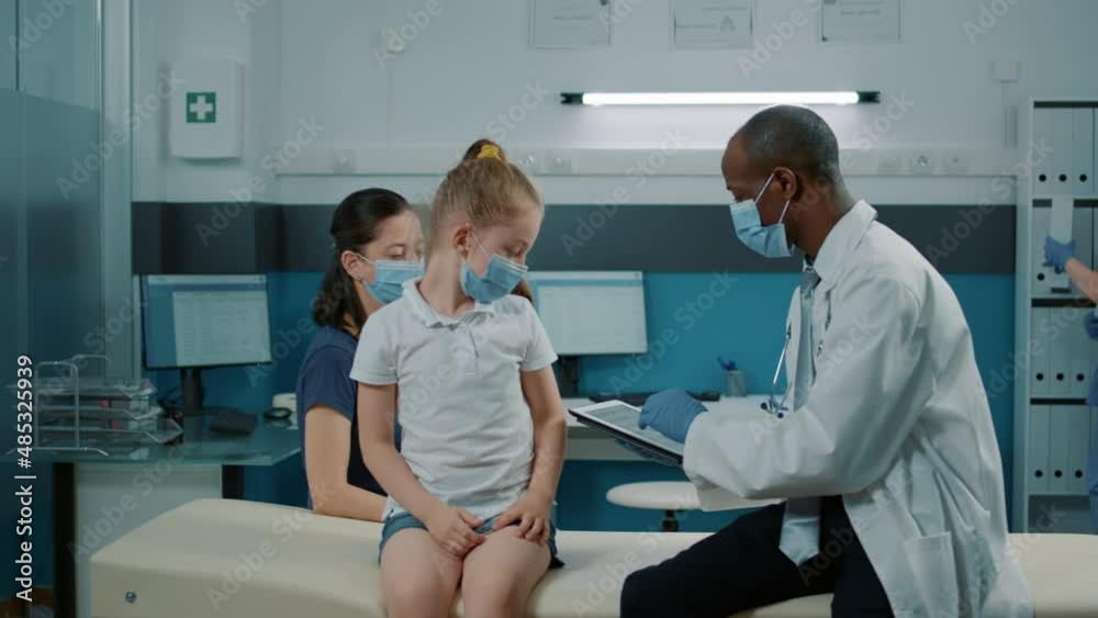 General practitioner using digital tablet to take notes at examination appointment in medical cabinet. Medic consulting little girl at checkup visit to help with health care treatment. General practitioner using digital tablet to take notes at examination appointment in medical cabinet. Medic consulting little girl at checkup visit to help with health care treatment.