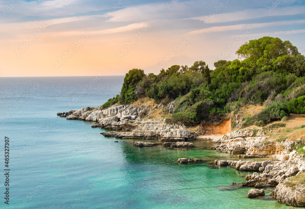Rugged coastline near Kassiopi resort on Corfu island, Greece. Picturesque seashore with cliffs and trees over turquoise water of Mediterranean sea. Popular tourist destination