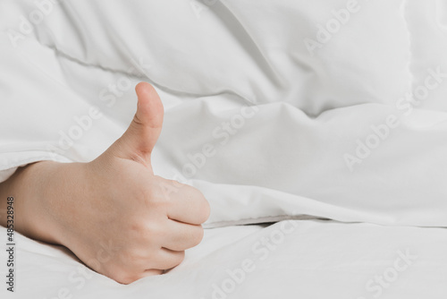 Childs hand with thumb up under white blanket. The warmth of home comfort.