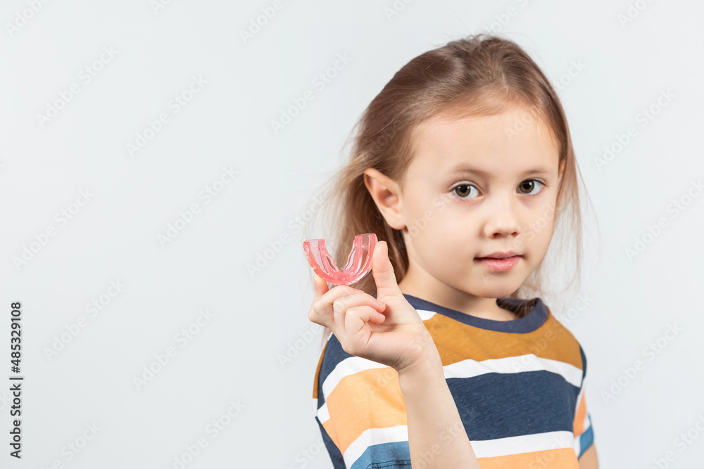 Cute little girl with blond hair is holding a pink dental myofunctional trainer Cute little girl with blond hair is holding a pink dental myofunctional trainer