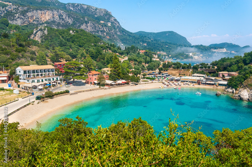 Paleokastritsa beach and village on Corfu island, Greece. Picturesque seashore with turquoise crystal water, pebble beach Agios Spiridon, mountains and cliffs