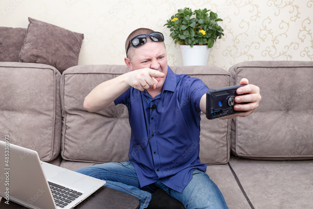 Fototapeta premium A man in a blue shirt blogs and takes a selfie on his phone.