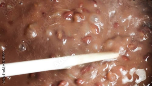 Stirring with the spoon in red beans cooking in the stone pot.