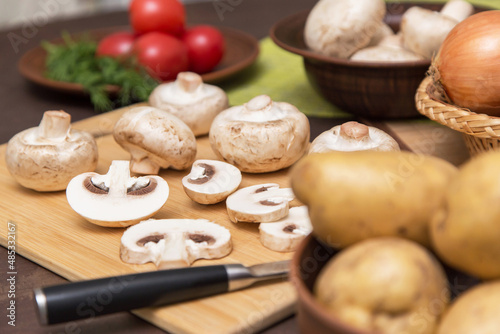 Sliced mushrooms champignon with vegetables on wooden cutting board on kitchen. Cooking vegetarian diet dish