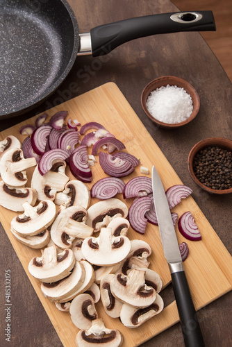Sliced mushrooms champignon with onion on wooden board with frying pan on kitchen. Cooking vegetarian dish