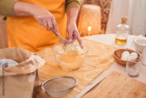 Caucasian elderly woman mixing ingredients with whisk into the bowl while cooking at the kitchen