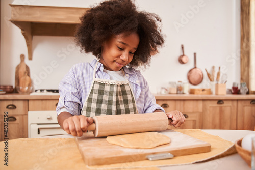 Multiracial child girl kneading dough and preparing doing bakery while cooking at the cozy kitchen