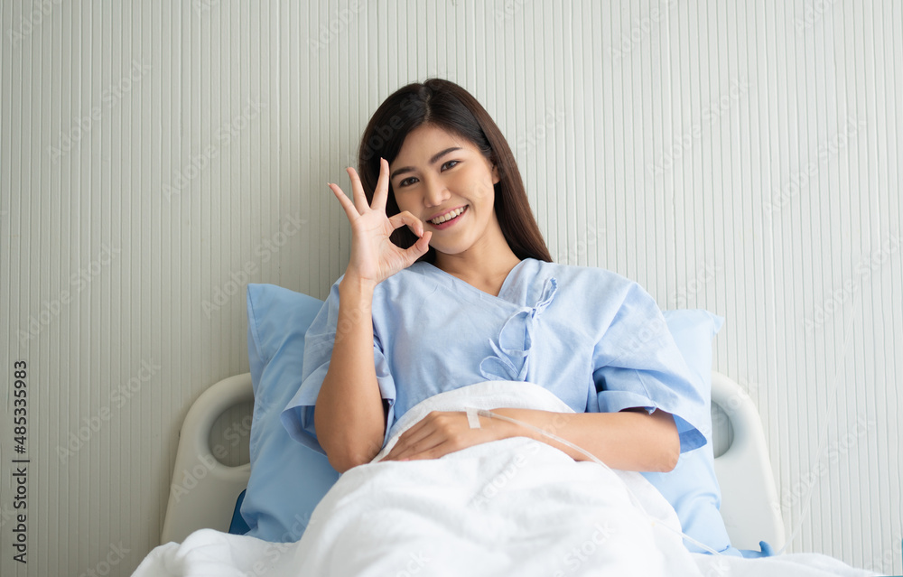 Happy Asian female patient smiling, lies on the bed, and Shows an ok symbol to show confidence in treatment. Concept of believe in treatment And insurance coverage Happy Asian female patient smiling, lies on the bed, and Shows an ok symbol to show confidence in treatment. Concept of believe in treatment And insurance coverage
