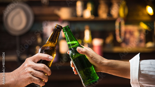two hands hold beer bottle toasting in bar