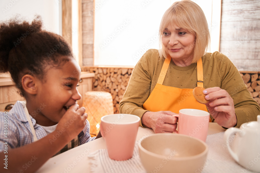 Portrait of smiling mother and kid reposing at the kitchen table with mugs in hands Portrait of smiling mother and kid reposing at the kitchen table with mugs in hands