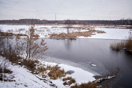 Winter landscape with a freezing river. View of the waterfall. The ice and the banks are covered with snow. Beautiful rural landscape.