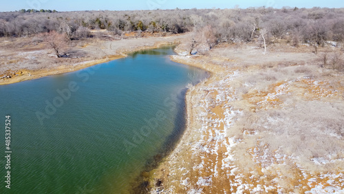 Top view snow covered rocky shoreline with dry tree stumps along crystal water of Lake Grapevine, Texas, USA