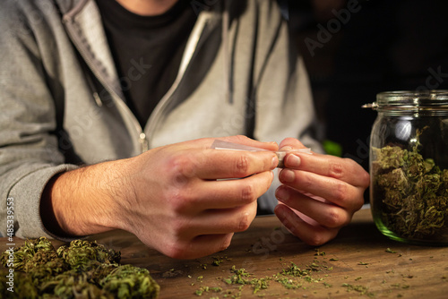 Canvas Print Man rolling marijuana cannabis joint in coffee shop Amsterdam with CBD weed buds in glass jars