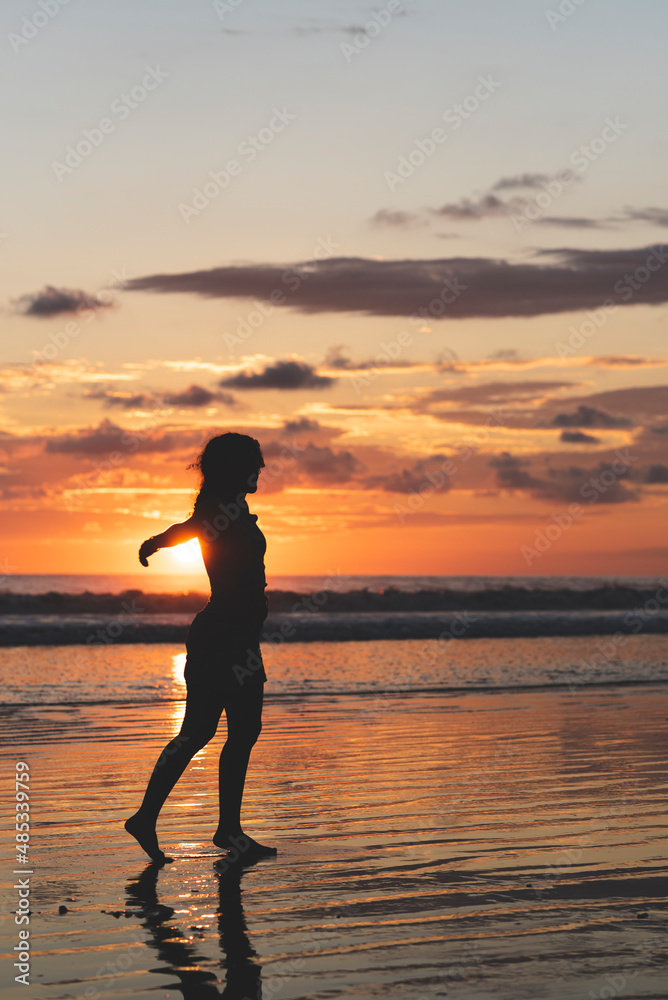 vertical portrait, Silhouette of a woman with open arms enjoying a sunset on a beach in Costa Rica.