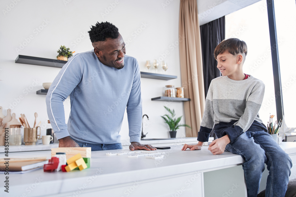 Multiracial father and his caucasian son communicating at the cozy kitchen Multiracial father and his caucasian son communicating at the cozy kitchen