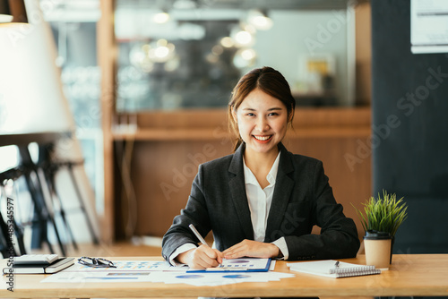 Confident young female financial advisor writing on diary while sitting with laptop at desk in office