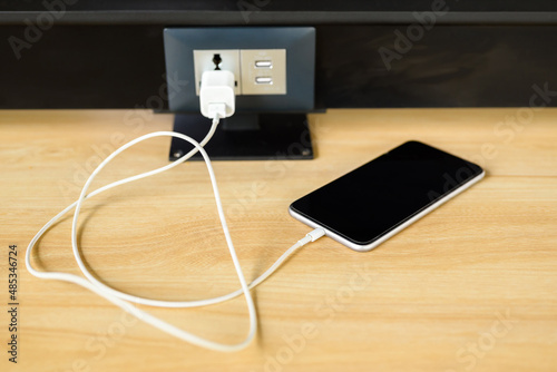 Mobile phone in charging from the USB adapter and electrical power socket on the table
