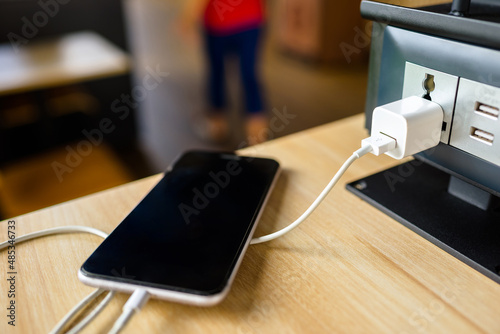 Closeup USB port and adapter at the electrical power socket on the table, phone during charging in the cafe photo