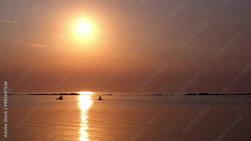 Two swimmers are kayaking on the sea and paddling at sunset under a bright sun disk Two swimmers are kayaking on the sea and paddling at sunset under a bright sun disk