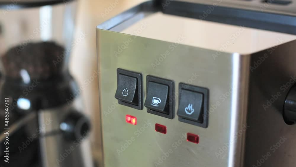 a person's hand presses a finger on the button for turning on an espresso coffee machine. close-up of household appliances made of steel. a person's hand presses a finger on the button for turning on an espresso coffee machine. close-up of household appliances made of steel.