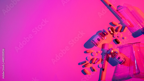 Covid-19 medication. Neon banner. Pharmaceutical manufacture. Color light vaccine bottle dose syringe pills test tube composition on bright pink purple copy space background.