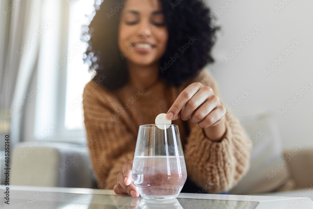 Closeup of a young woman dropping an effervescent antacid in a glass of water. young woman hardly put a soluble pill with a medicine for pain or a hangover in a glass of water Closeup of a young woman dropping an effervescent antacid in a glass of water. young woman hardly put a soluble pill with a medicine for pain or a hangover in a glass of water