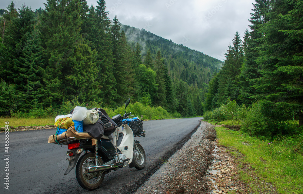 Asphalt empty road in coniferous mountains, traveler's bike moped by roadside, freedom and journey concept Asphalt empty road in coniferous mountains, traveler's bike moped by roadside, freedom and journey concept