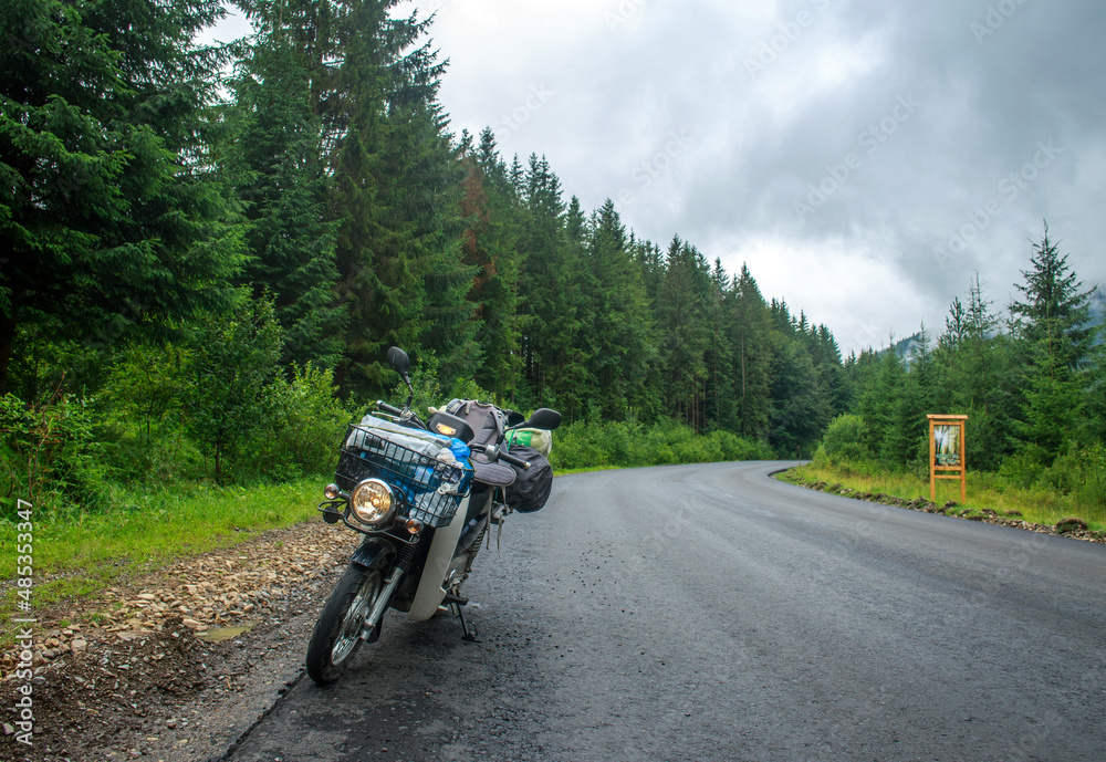 Asphalt empty road in coniferous mountains, traveler's bike moped by roadside, freedom and journey concept
