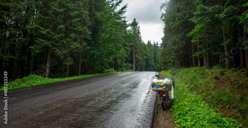 Asphalt empty road in coniferous mountains, traveler's bike moped by roadside, freedom and journey concept photo