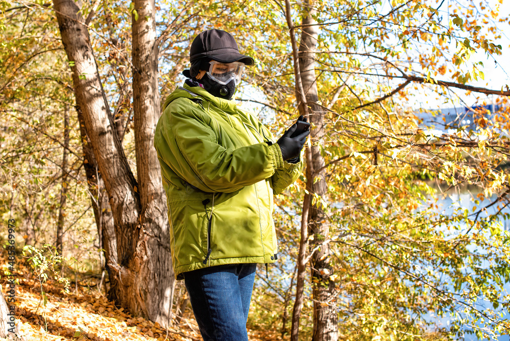 A woman in rubber gloves using a smartphone walking in the forest at COVID-19 period.