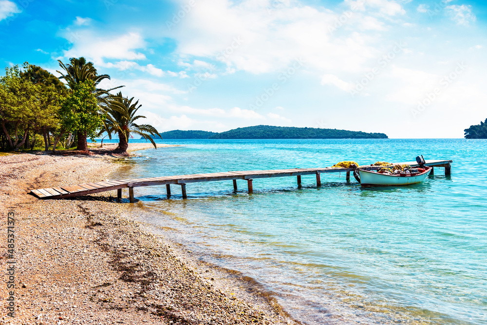 Fascinating optimistic seascape with palms and a boat near wooden pier on a tropical beach.