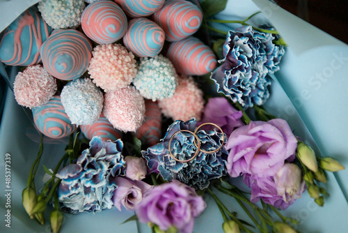 Wedding rings lie on a bouquet of sweets and flowers