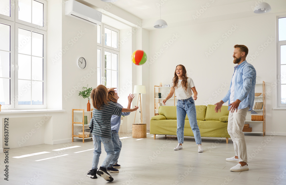 Happy family playing ball in the house. Cheerful young mother, father and little children playing football at home. Mommy, daddy and kids playing soccer with a toy ball and having lots of fun together