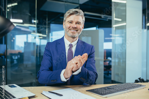 An experienced manager looks at the camera and smiles, a businessman claps his hands on a video call, as a sign of praise and support to interlocutors