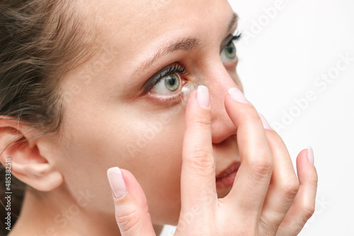 Cropped shot of a young woman applying eye lens with her hand isolated on a white background. The girl wearing contact lenses. Beauty, vision, ophthalmology