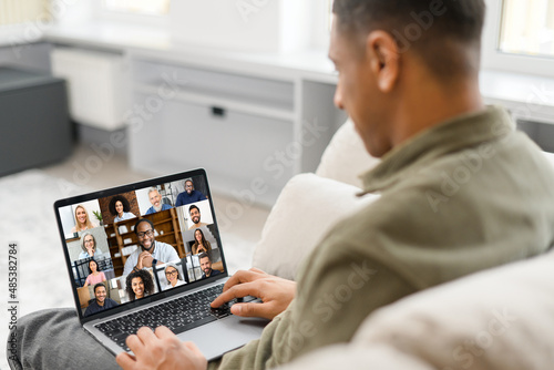Cropped view of the multiracial man in casual wear sitting on the comfortable sofa and using trendy laptop for video call with many interlocutor. Virtual meeting, video call concept
