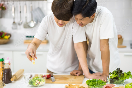 Asian gay couple cook salad together in kitchen