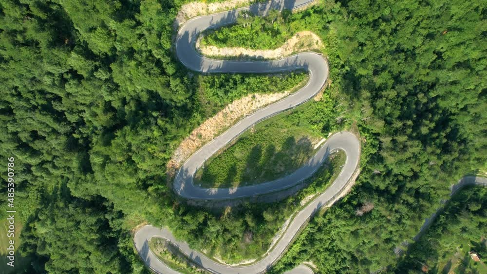 AERIAL, TOP DOWN: Empty switchback road snakes up a hill and through a lush green forest. Flying above an asphalt mountain road full of sharp hairpin turns running across the vibrant woods of Slovenia