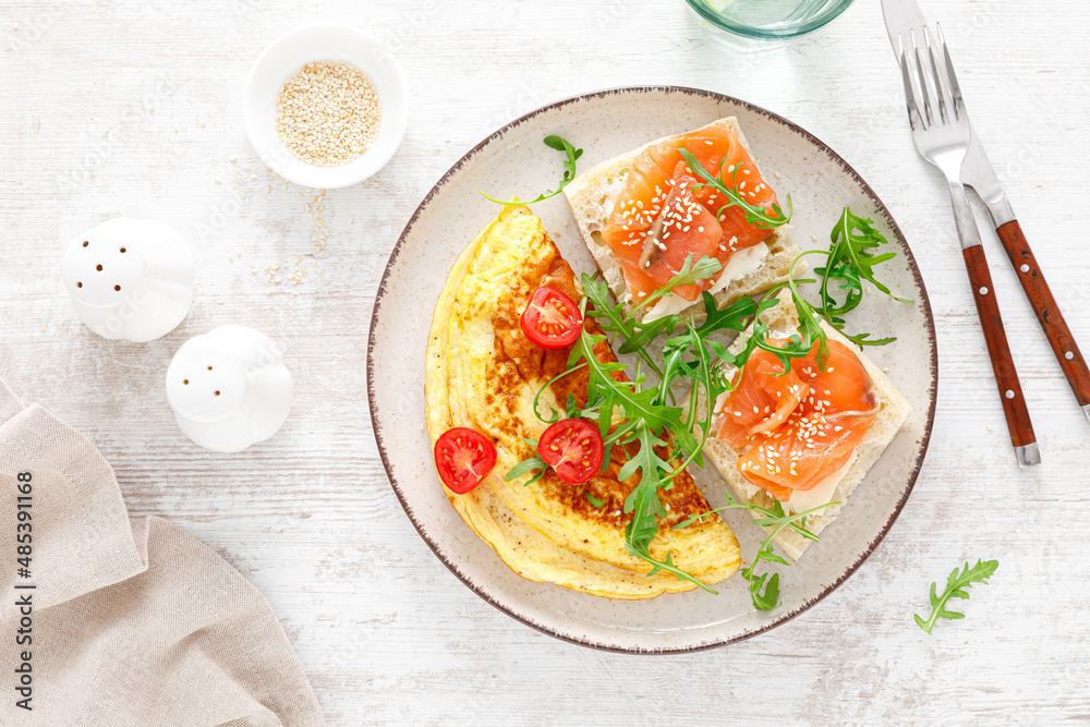 Omelette or omelet, fresh arugula and tomato salad and toasts with butter and salted salmon. Breakfast. Top view Omelette or omelet, fresh arugula and tomato salad and toasts with butter and salted salmon. Breakfast. Top view