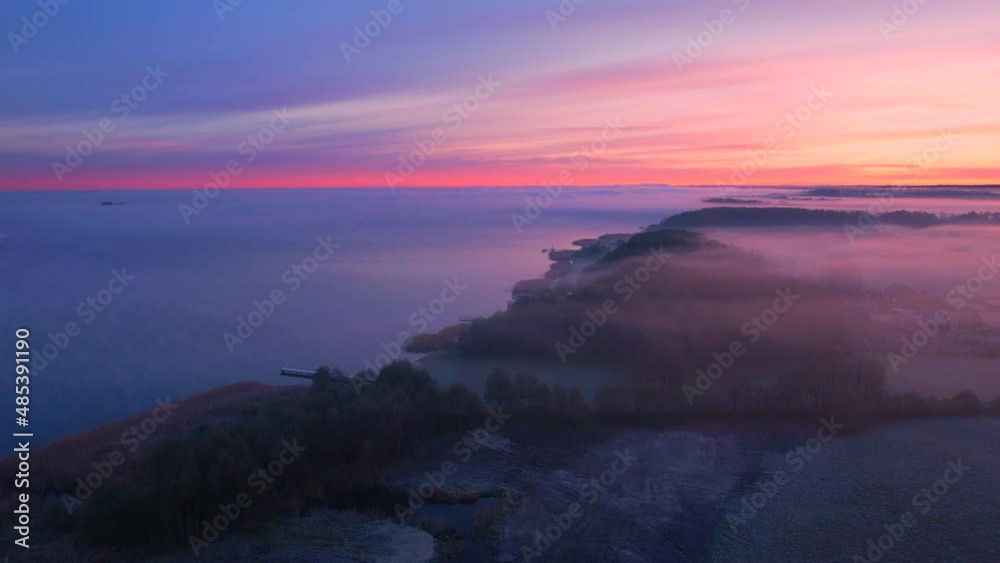 Aerial view of the foggy morning at the lake. Beautiful sunrise, pastel pink clouds and orange sun. Slow drone flight, zoom out. Aerial view of the foggy morning at the lake. Beautiful sunrise, pastel pink clouds and orange sun. Slow drone flight, zoom out.